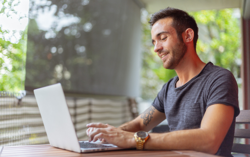 Smiling entrepreneur working on a laptop outdoors, showcasing the freedom and flexibility of earning passive income online.